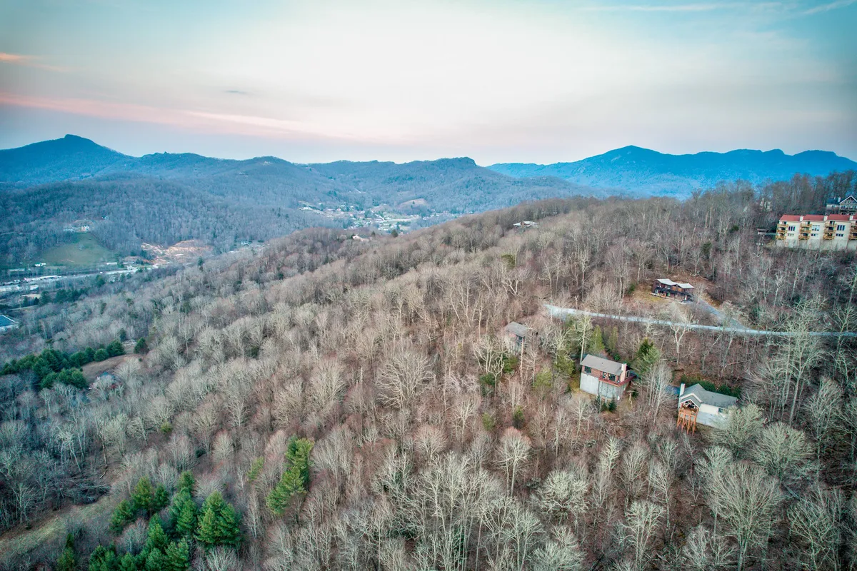 A panoramic view of a mountain range with tree-covered hills and scattered homes, evoking a sense of exploration and connection with nature. The vista suggests a perfect environment for walks, hikes, and peaceful moments amid scenic beauty.