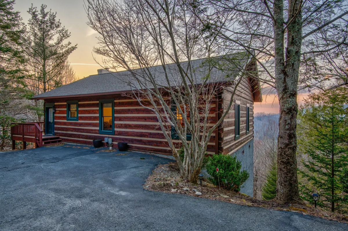 A warm, inviting view of the cabin exterior during twilight, with glowing windows and surrounding trees. The scene conveys privacy, a cozy retreat, and direct access to nature—perfectly encapsulating the idea of a romantic hideaway in the mountains.
