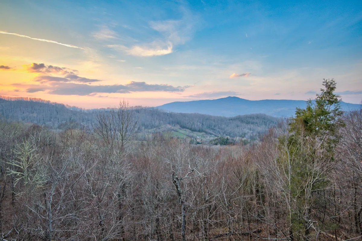 A wide, scenic view of distant mountains and bare trees beneath a dramatic sunset sky. The mood is serene, evoking the beauty and adventure of the surrounding area.