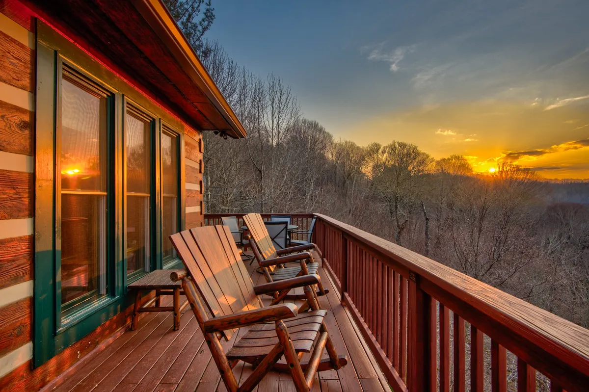 This image features the log cabin's exterior, perfectly framed by a pair of wooden rocking chairs on the porch and set against a dramatic sunset sky. The cabin's rustic architecture and the inviting chairs create a welcoming family gathering spot to unwind and share stories after a day of mountain fun.