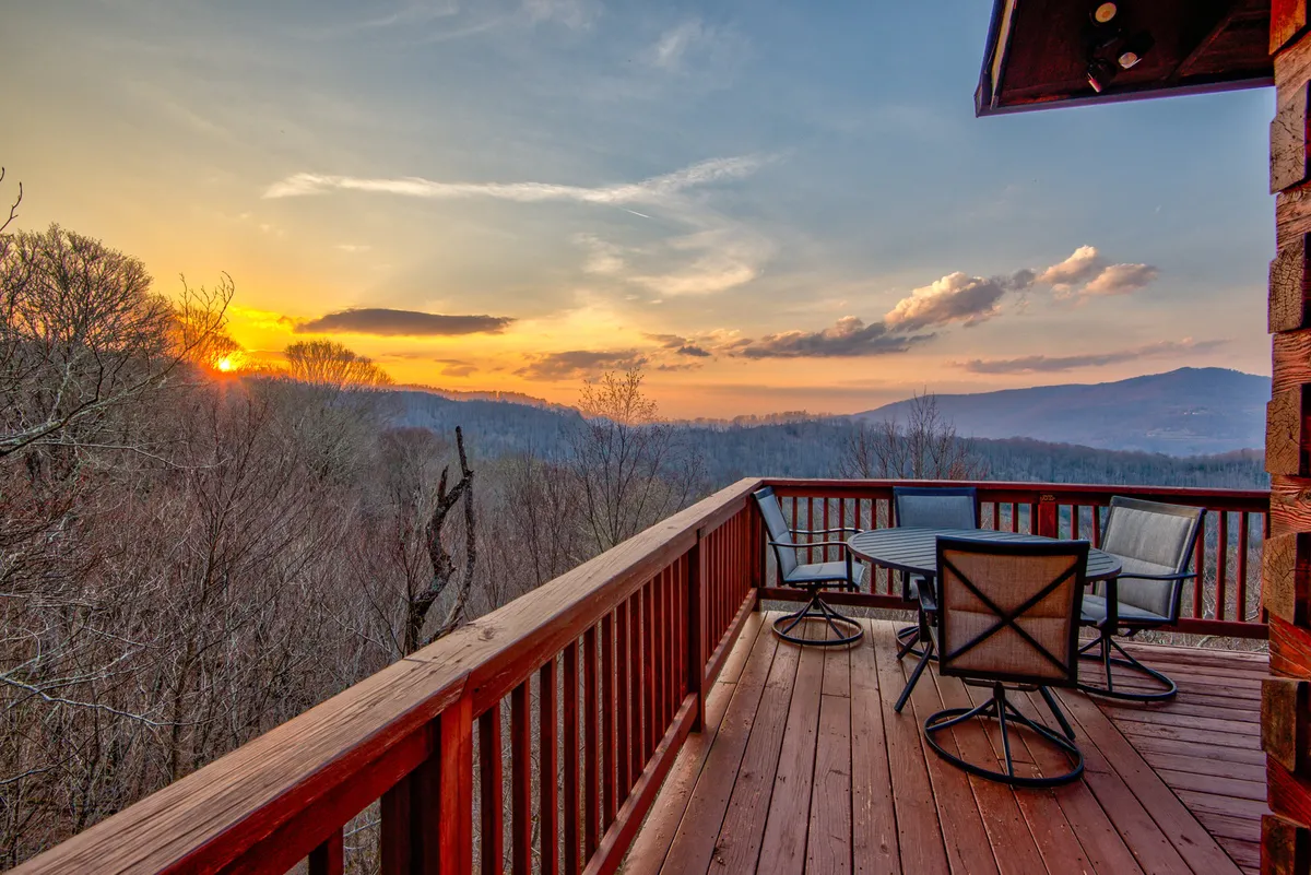 An outdoor seating area with a panoramic view of the sunset and rolling mountains, inviting couples to gather, sip wine, or simply enjoy the moment. The mood is tranquil and contemplative, with nature at its most scenic and romantic.