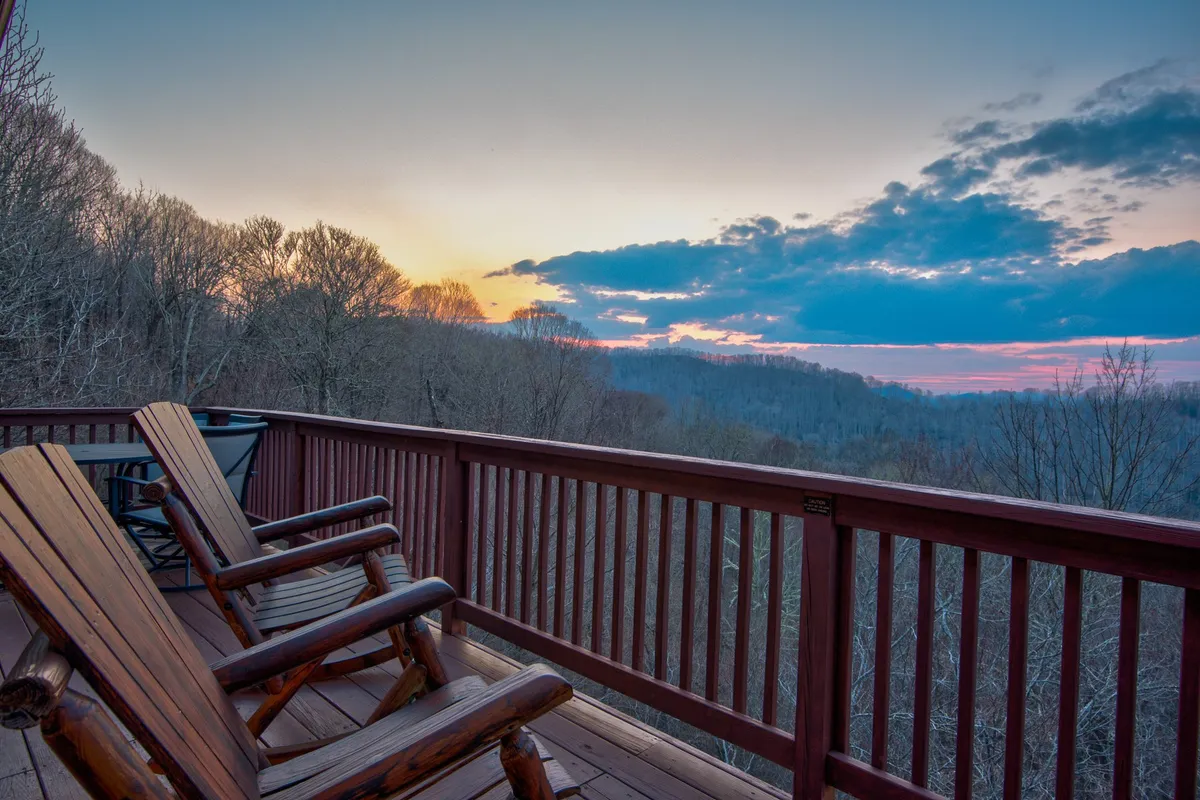 A tranquil scene with wooden rocking chairs positioned on a deck or porch, overlooking a sunset horizon and surrounded by nature. The space invites groups to sit together, unwind, and enjoy the view.