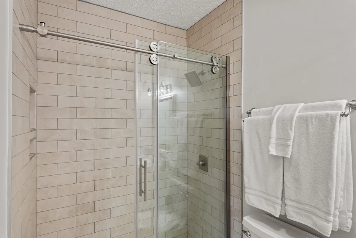 A bright, modern bathroom with a glass shower enclosure, sleek neutral tile, and inviting fixtures. The space feels clean and serene, ideal for refreshing morning routines or winding down at night.