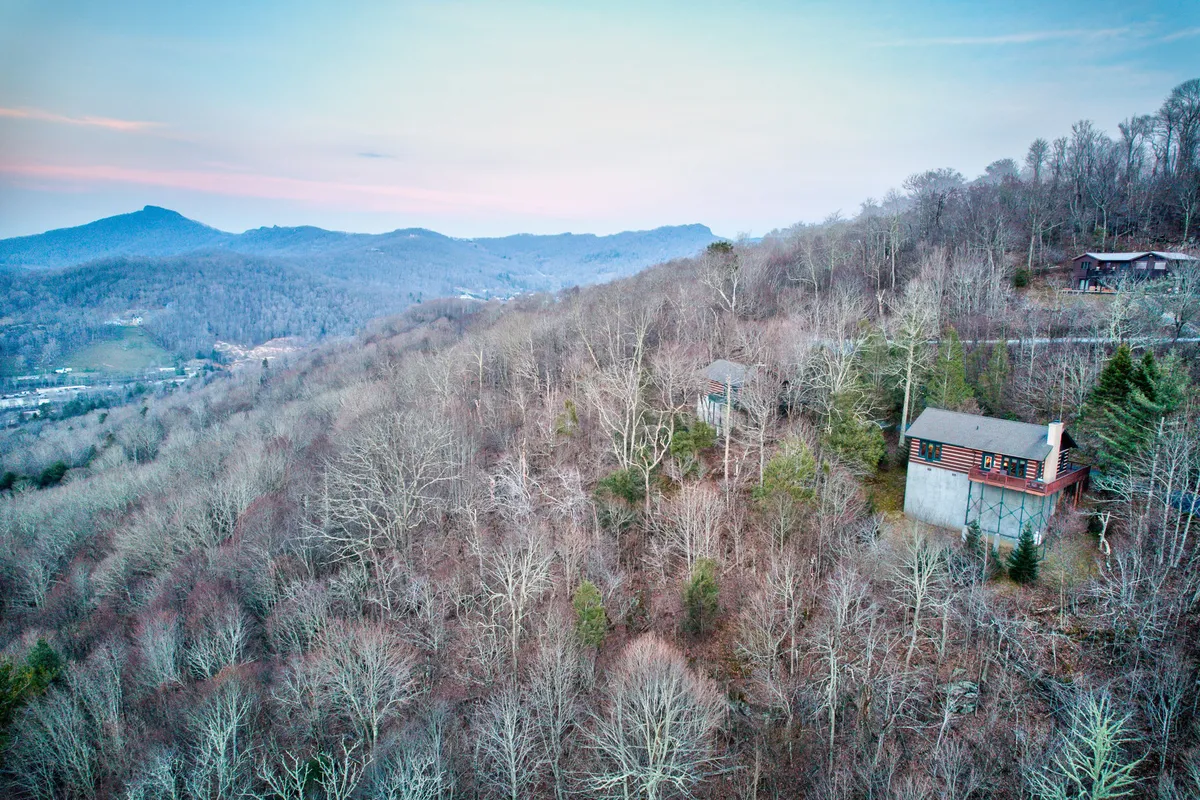 This image highlights a stunning mountain range with dense trees and a cozy cabin in the foreground, echoing the adventure and exploration theme with lush, hike-inspiring scenery.