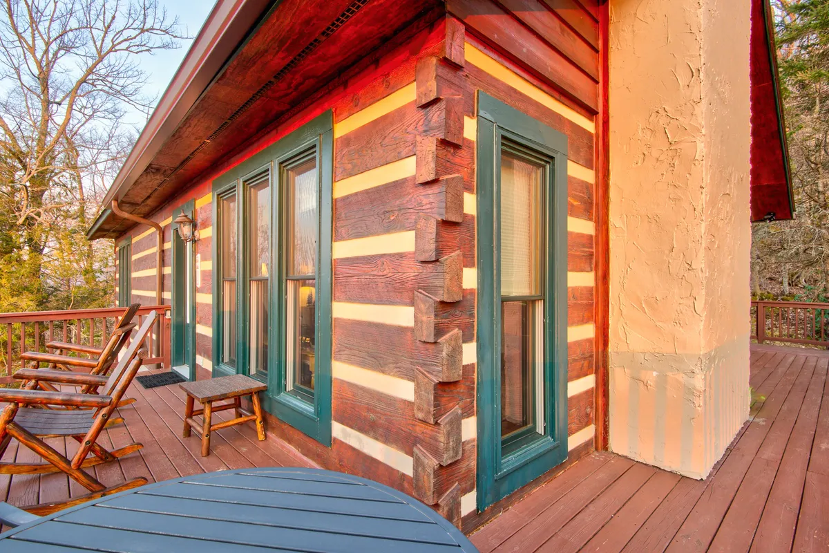 An exterior image showing the log cabin structure with large windows and a spacious deck area. The scene is peaceful and inviting, with hints of morning or evening relaxation possible on the deck.