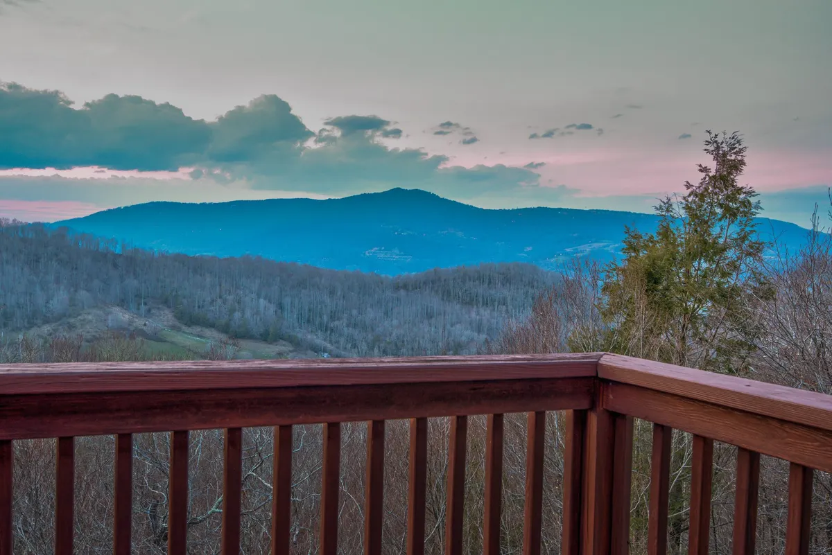 The image offers a breathtaking mountain vista as seen from a wooden deck. The sky is painted with sunset colors, and the view stretches over rolling peaks and valleys, evoking the thrill of mountain exploration and relaxation alike.