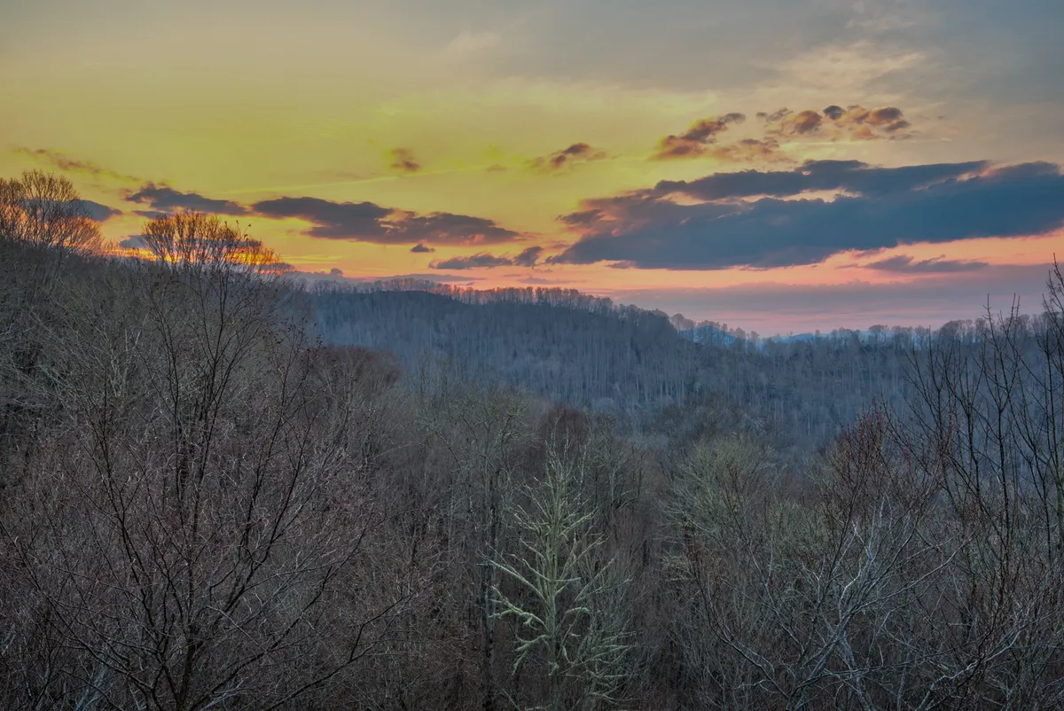 A stunning landscape at sunset, with vibrant clouds illuminating the sky above rolling mountains. The image invites thoughts of tranquil evenings outdoors and capturing memorable moments while surrounded by natural beauty.