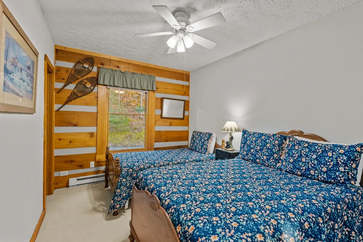 An inviting twin/full bedroom with two large beds adorned with floral bedding, wooden wall accents, a window letting in sunlight, and decorative snowshoes adding a mountain flair. The space feels warm and welcoming, ideal for families or friends sharing the room.
