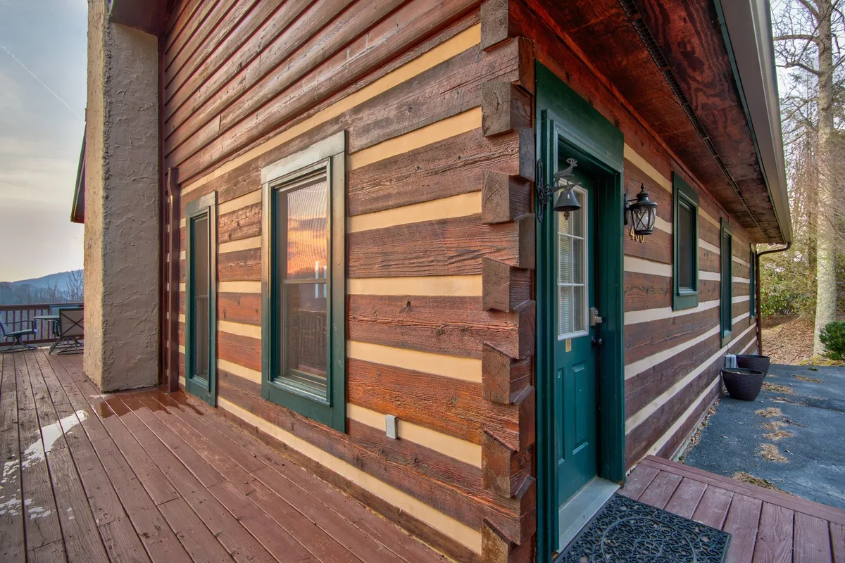 This image captures the exterior of the log cabin at sunset, with warm light reflecting in the windows and a green door welcoming guests. The inviting porch suggests a spot for group gatherings, sunset watching, or relaxing with friends after a day of adventure.